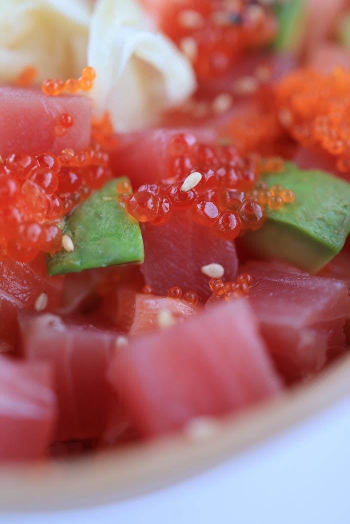 Vibrant sushi poke bowl featuring tuna, avocado, roe, and sesame seeds in a close-up shot.