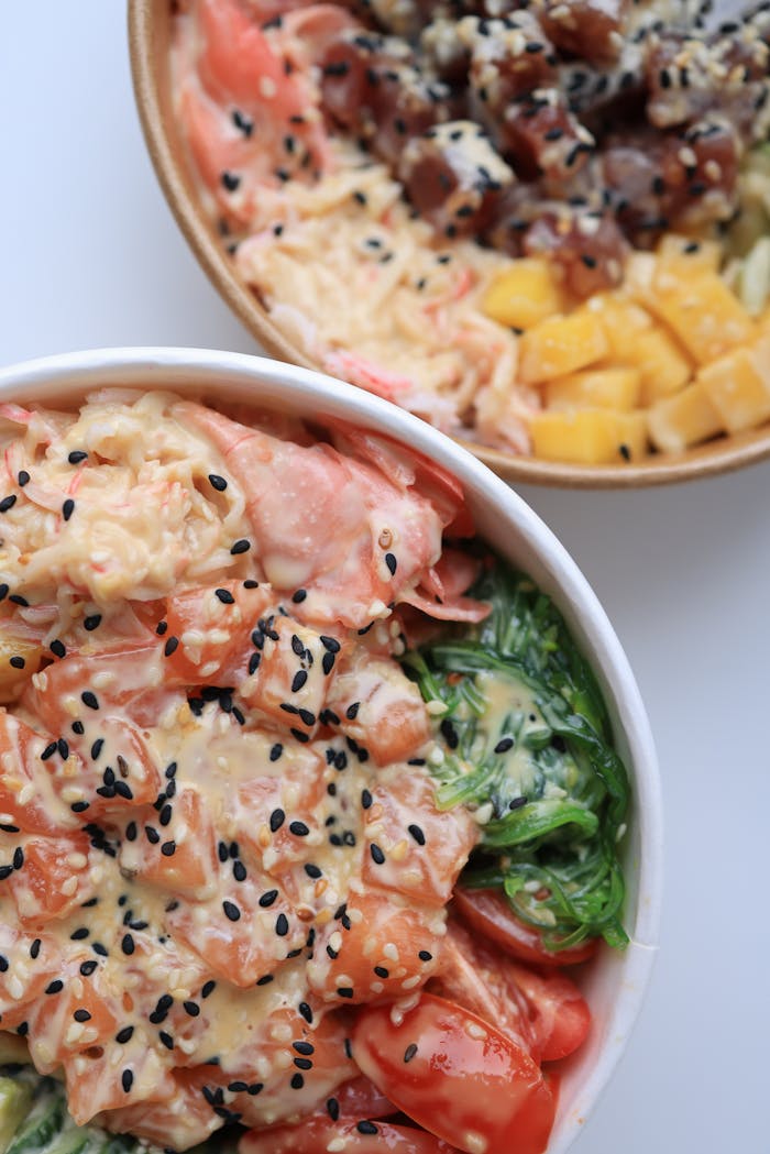 Delicious poke bowls with fresh salmon, tuna, mango, and seaweed, topped with sesame seeds.