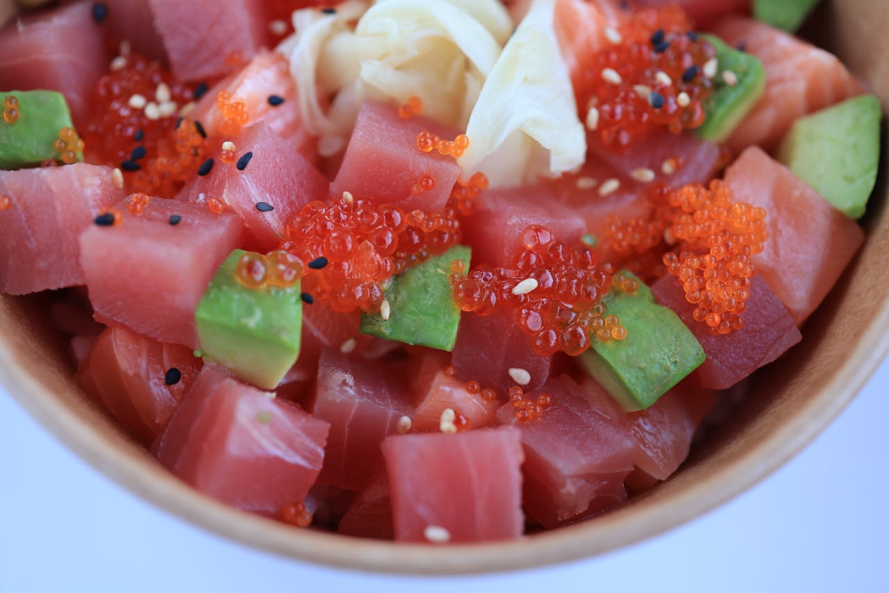 Colorful poke bowl with tuna, avocado, red caviar, and sesame seeds in a wooden bowl.