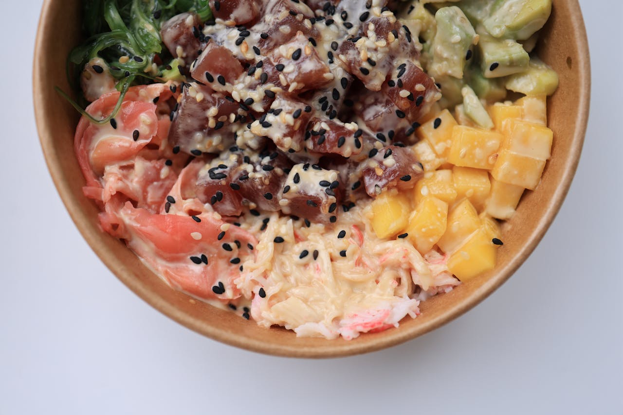 Delicious poke bowl filled with fresh tuna, mango, avocado, and seaweed on a white background.