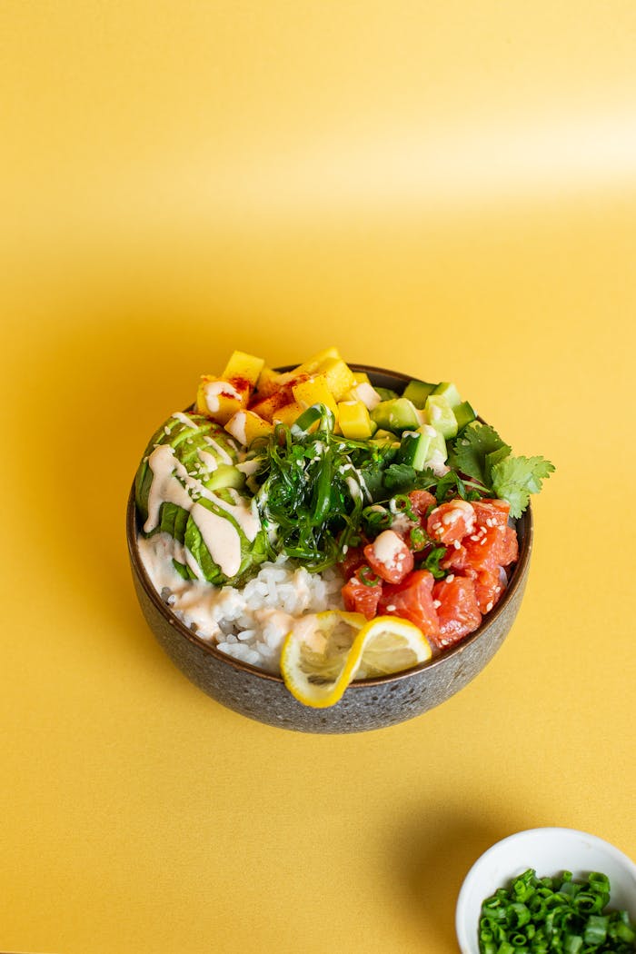 Colorful Hawaiian poke bowl with fresh ingredients on a vibrant yellow backdrop.